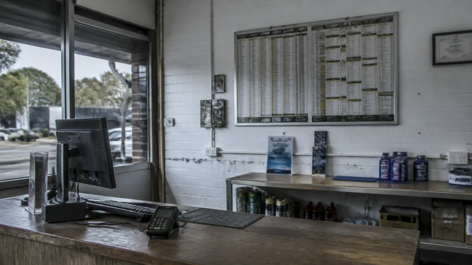 A small trade business front counter with a printed price board mounted on the wall behind it.